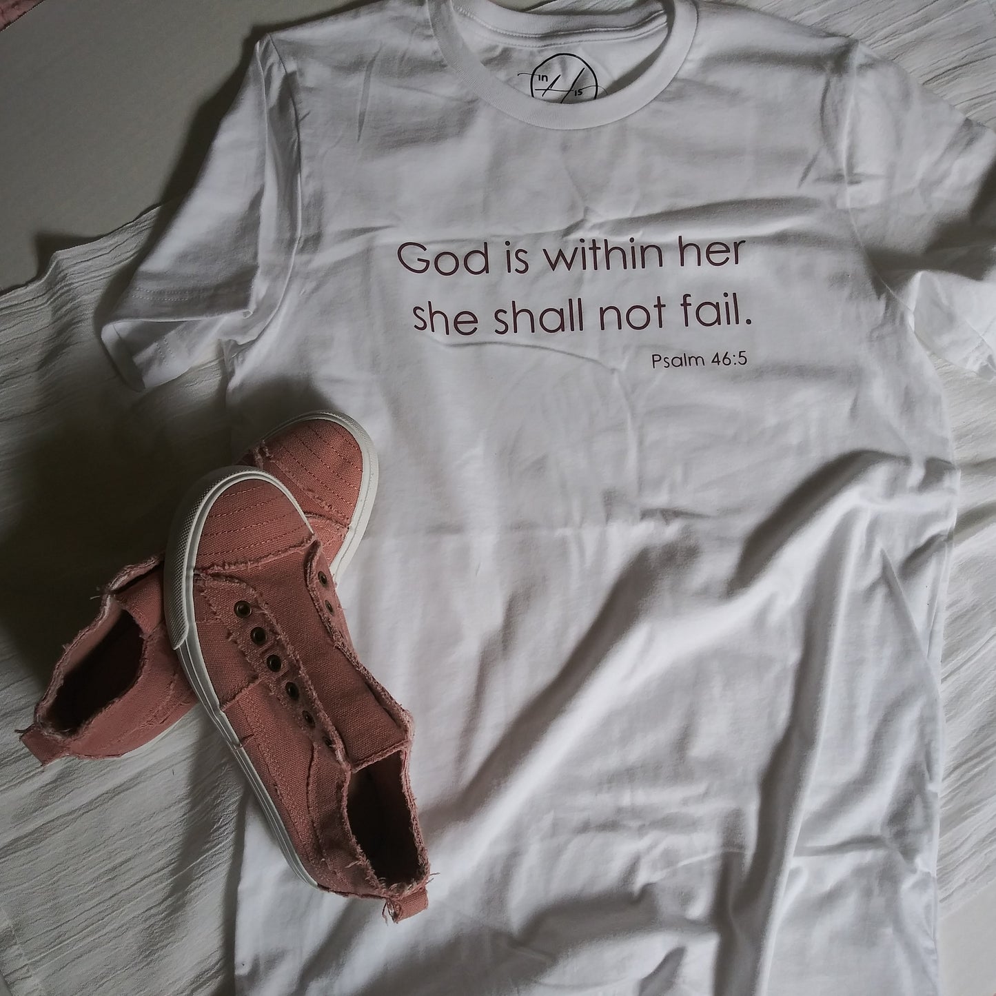 White t-shirt with Mauve reflective lettering: God is within her, she shall not fail (Psalm 46:5) on front, upper-middle.