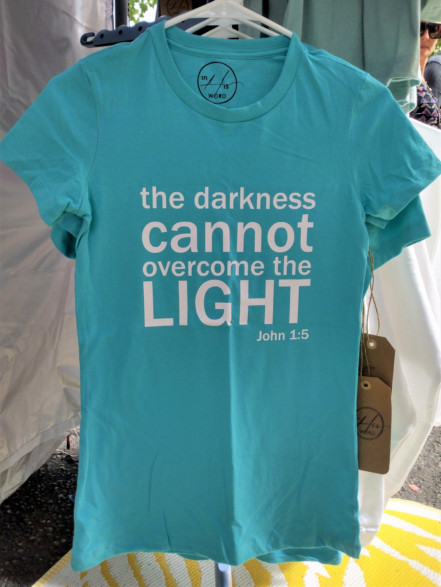 Teal ladies' junior fit t-shirt with white text "the darkness cannot overcome the light. John 1:5" on upper center of shirt.