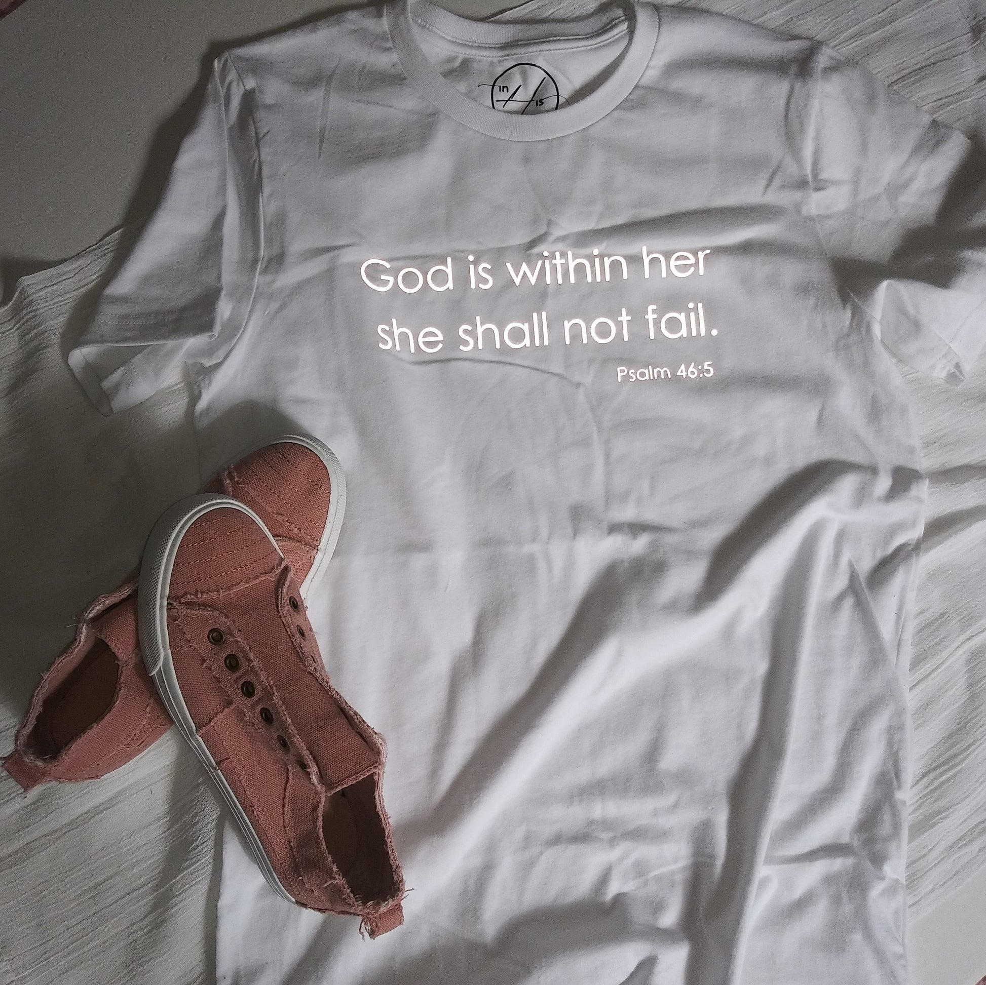 Reflective lettering: God is within her, she shall not fail (Psalm 46:5) on front, upper-middle of white t-shirt. 